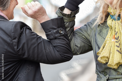 Elbow bump. New novel greeting to avoid the spread of coronavirus. Two women friends meet in a British street and instead of greeting with a hug or handshake, they bump elbows instead.