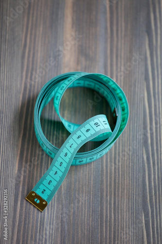 Sewing accessories – the green centimetric measuring tape, tailor tape on a wooden background