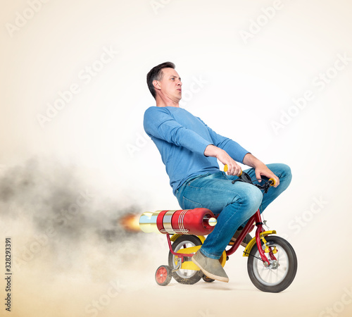 Cool man in casual wear rides a children's bike with alternative rocket engine. On a light yellow background. photo
