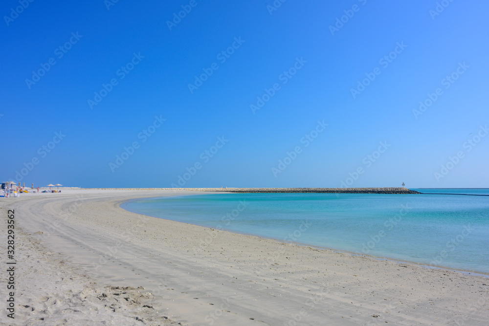 Beautiful summer curve sand beach with rocks pier over turquoise sea blue sky and tourist taking sunbath background in Bahrain.