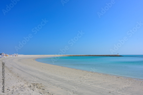 Beautiful summer curve sand beach with rocks pier over turquoise sea blue sky and tourist taking sunbath background in Bahrain.