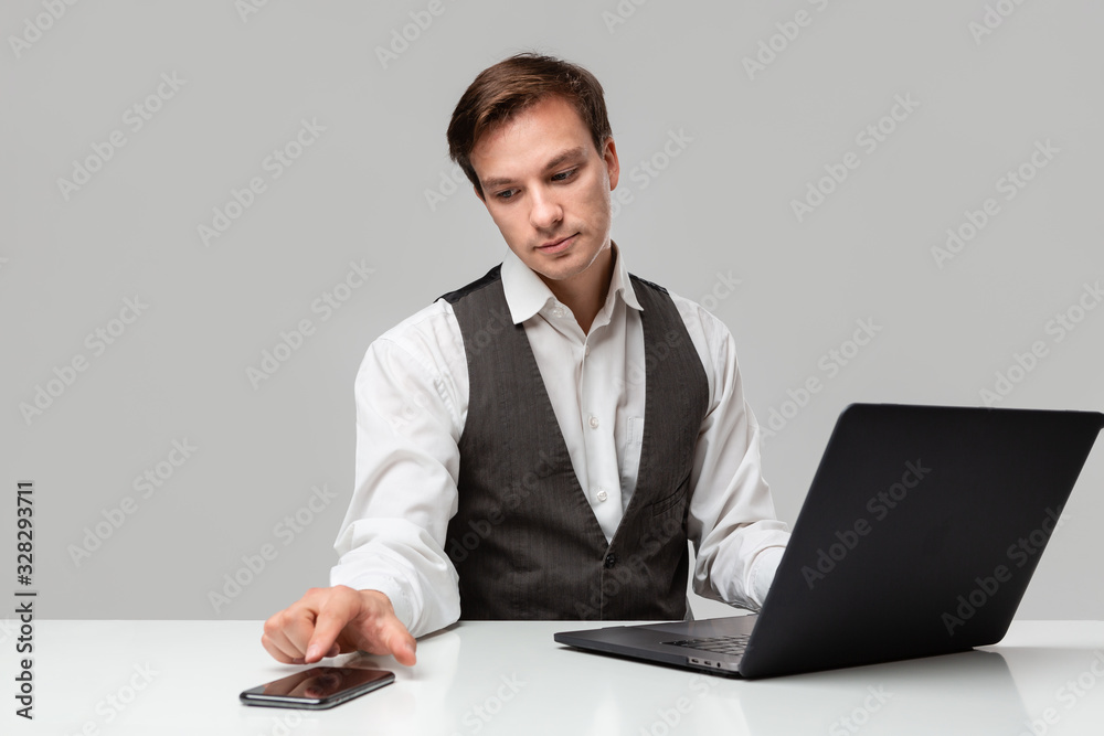 Businessman in a white t-shirt and grey vest working on a laptop. Man looking at the camera Businessman in a white t-shirt and grey vest working on a laptop. Man looking at the camera