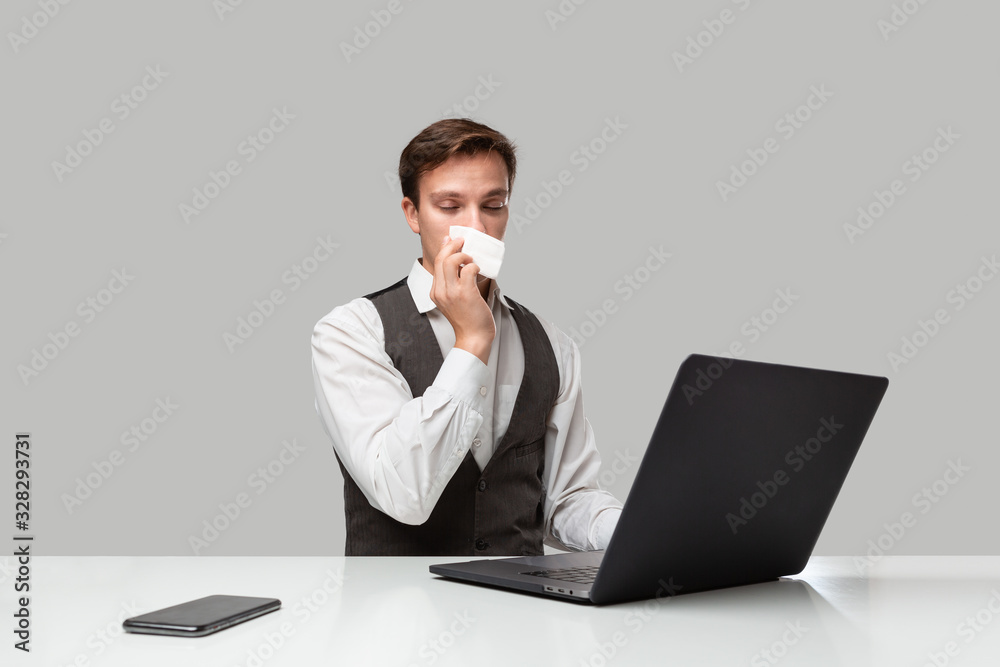 Businessman in a white t-shirt and grey vest working on a laptop in spite of running nose Businessman in a white t-shirt and grey vest working on a laptop in spite of running nose