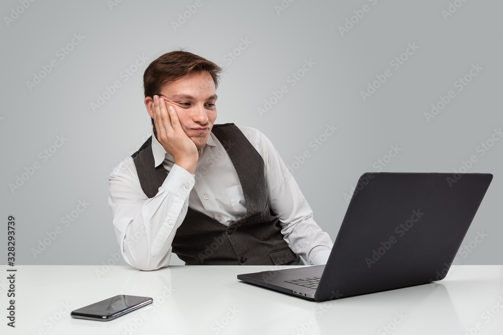 Businessman in a white t-shirt and grey vest is bored and looking at the screen of a laptop Businessman in a white t-shirt and grey vest is bored and looking at the screen of a laptop