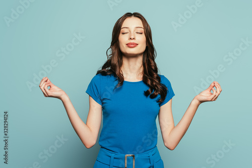 smiling girl standing in meditation pose with closed eyes on blue background