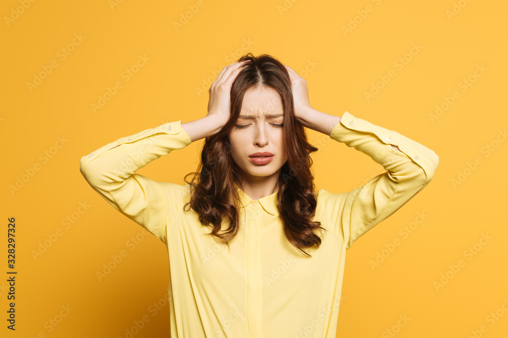 tired girl touching hand with hands while suffering from headache with closed eyes on yellow background tired girl touching hand with hands while suffering from headache with closed eyes on yellow background