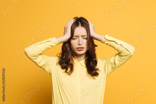 tired girl touching hand with hands while suffering from headache with closed eyes on yellow background
