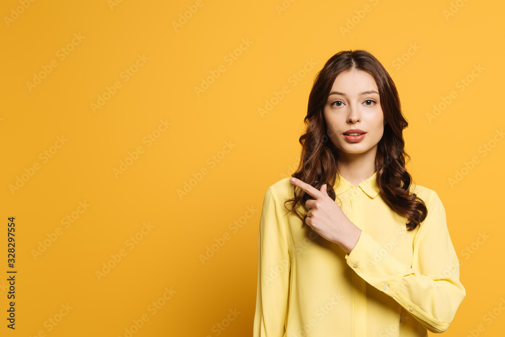 serious, attractive girl looking at camera and pointing with finger on yellow background serious, attractive girl looking at camera and pointing with finger on yellow background