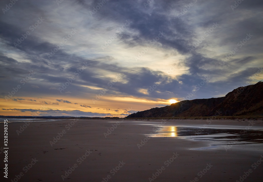 A dramatic Winter Sunset over an empty St Cyrus beach on a cold February Evening with reflections in the wet sand.