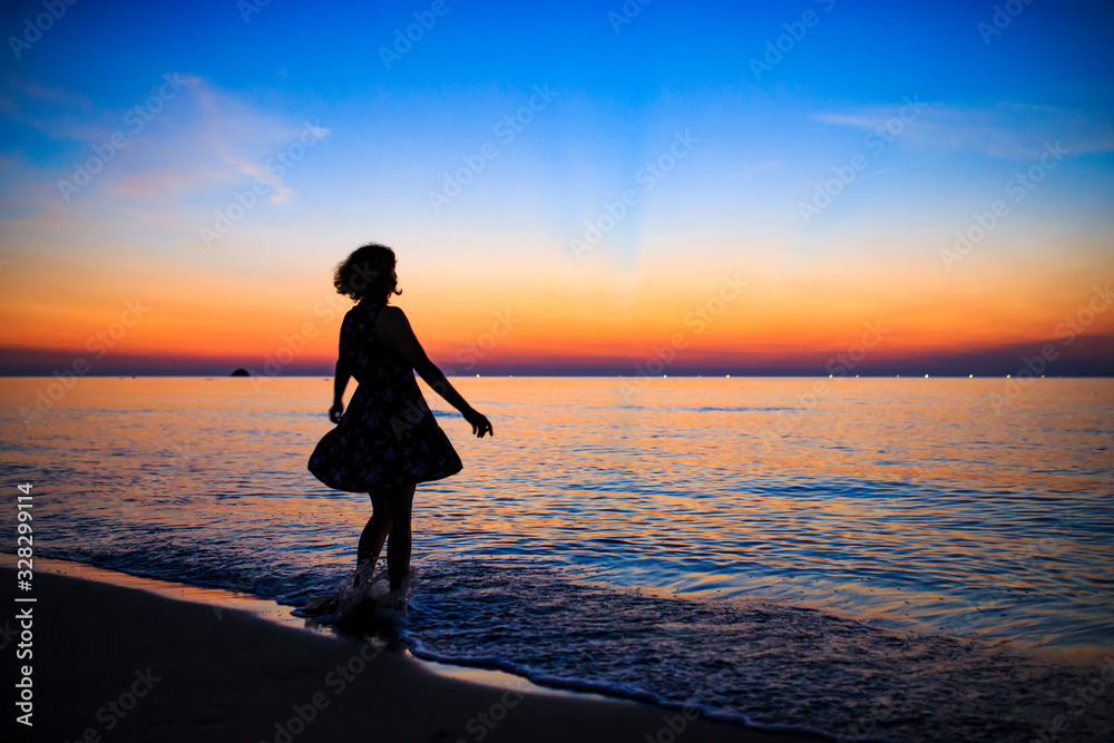 夕暮れの海辺に立つ白人女性
