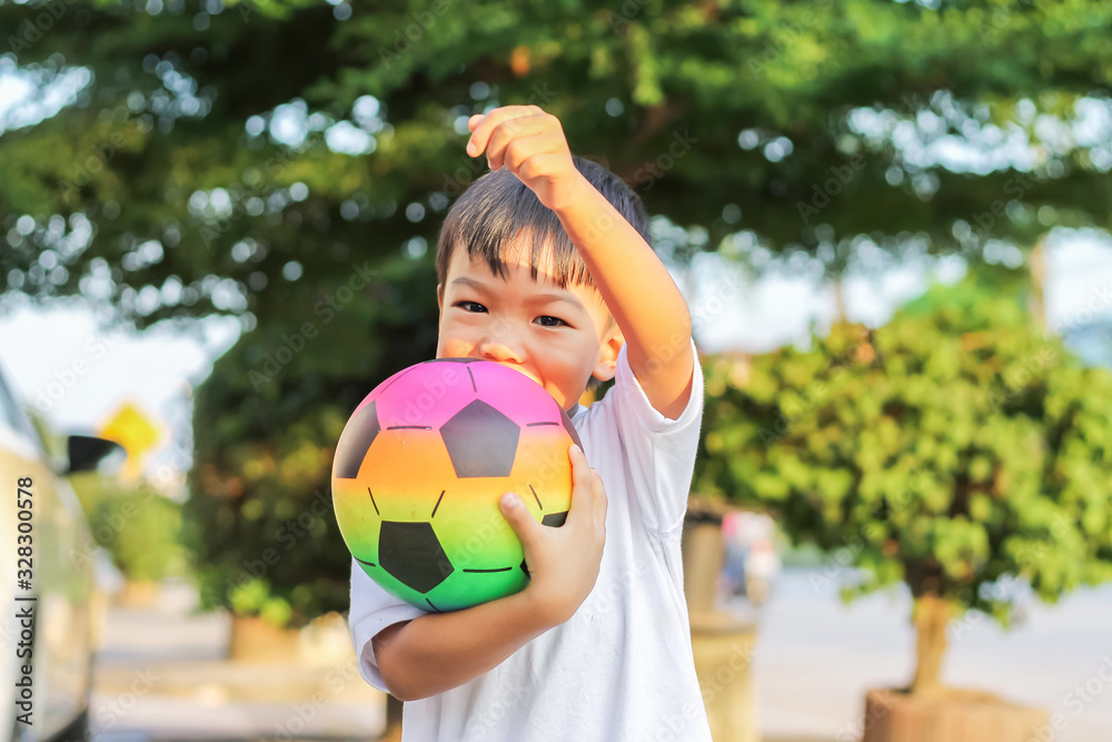 Portrait image of 5-6 boy. Happy Asian child boy playing and holding a football toy in his hands. He wear white shirt at the field playground. Happy and smiling boy. Sport and kid concept.