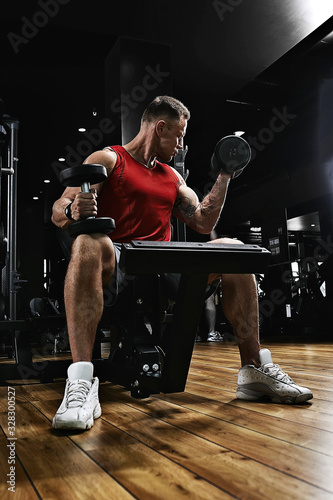 Muscular guy bodybuilder doing exercises with dumbbells in the gym. Athletic body, healthy lifestyle, fitness motivation, body positive.