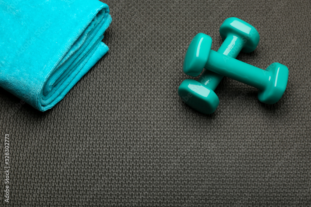 fitness concept. lightweight turquoise dumbbells and towel on the background of a black sport mat. 