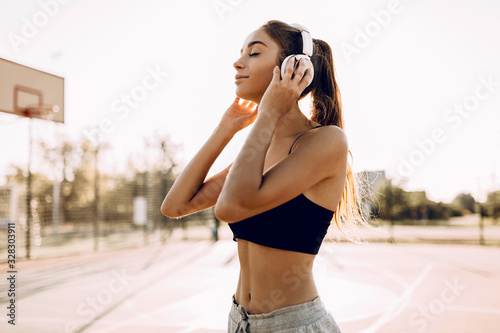 Happy athletic young woman, in sportswear, standing outdoors and listening to music with headphones © Shopping King Louie