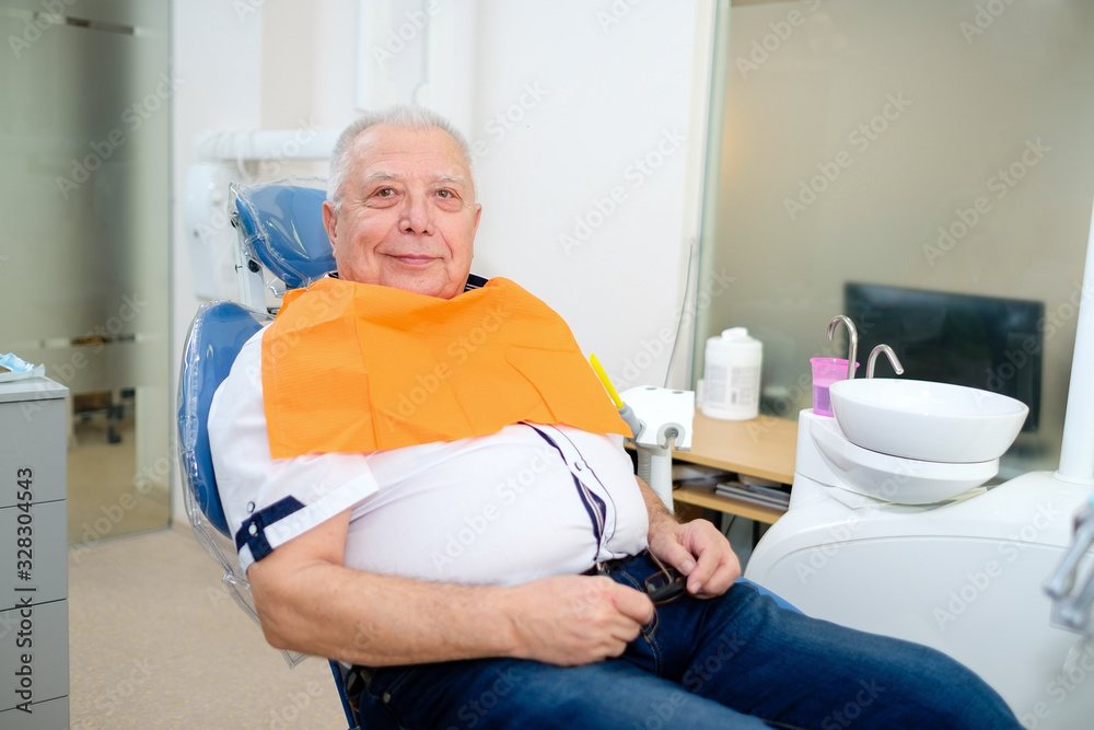 Obraz premium Portrait of happy senior man patient 70-75 years old. Male sitting on armchair at dental clinic. Dentistry, medicine and health care concept. Dental care for elder people.