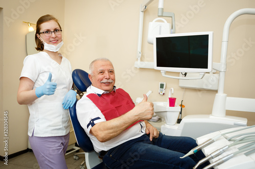 Smiling elderly man and young woman dentist after teeth treatment