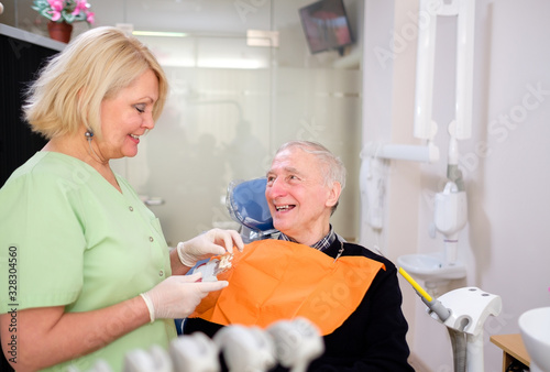 Mature woman dentist doing dental treatment of senior male 70-75 years old patient in dental clinic. Dental care for older people. Dentistry, medicine and health care concept