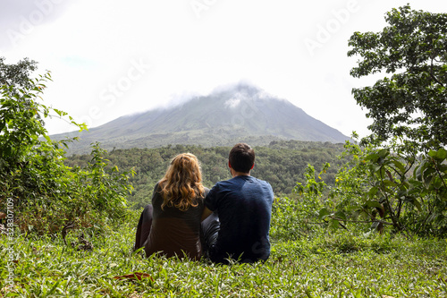 back of Young couple looking at Arenal volcano, sitting on green grass and enyojing nature, Costa Rica, Central America, la fortuna
