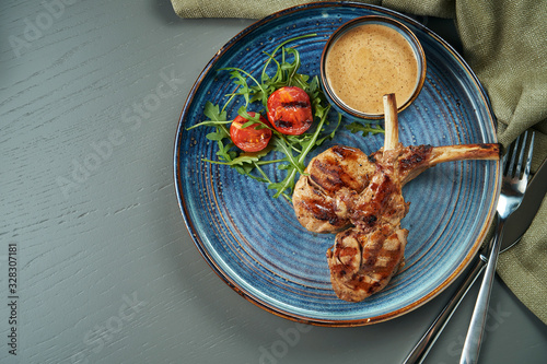 A grilled rack of young calf or lamb (beef) with peanut sauce and cherry tomatoes in a blue plate on a wooden background. Top ivew, flat lay photo