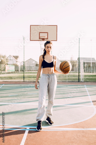 Beautiful young sporty girl playing with the ball on the basketball court outdoors.