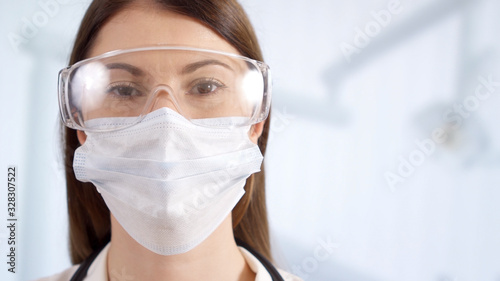 Portrait of professional female doctor in mask standing in hospital room. Woman physician at work