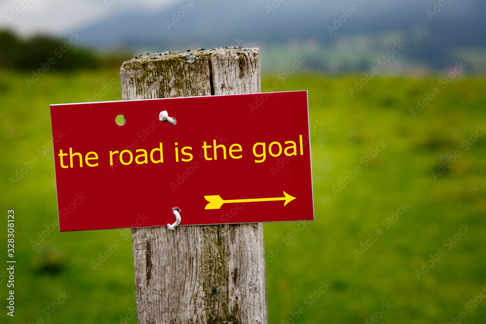 red sign in the alps with the text: the road is the goal