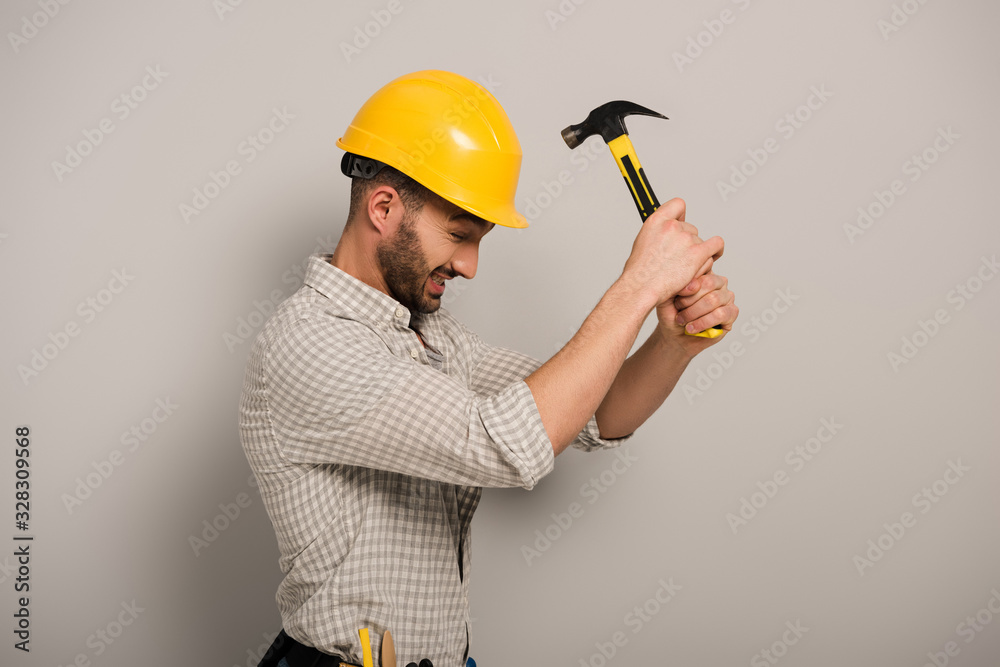 stressed workman beating yellow helmet with hammer on grey stressed workman beating yellow helmet with hammer on grey