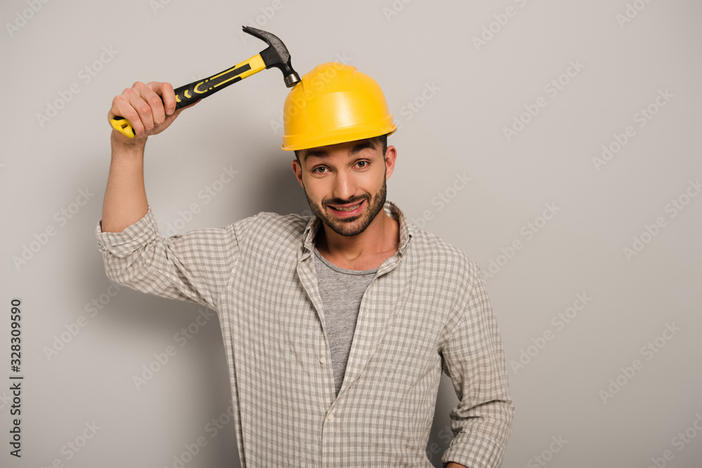confused repairman in helmet holding hammer on grey confused repairman in helmet holding hammer on grey