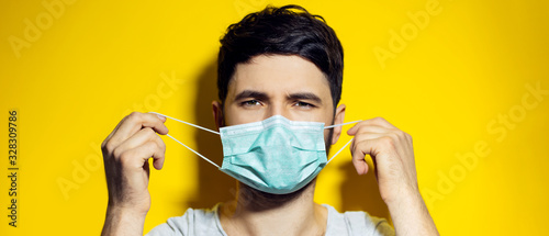 Close-up portrait of young man, takes off the medical protective flu mask, on background of yellow color.
