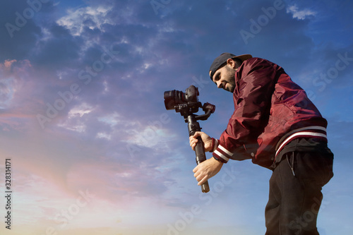 Caucasian videographer filming with cinema gimbal video dslr at sunset , professional video, video maker in event. Cinema lens on gimbal. Medium shot low angle photo