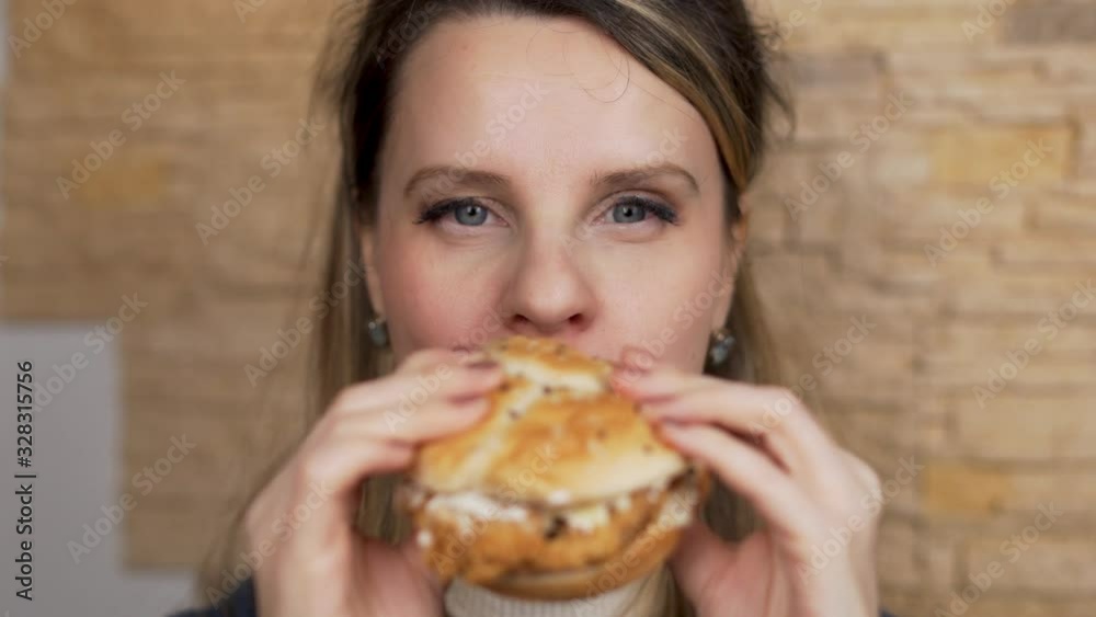 Close- up of a Woman eating a Burger with an Appetite and Looking at the Camera. Close- up of a Woman eating a Burger with an Appetite and Looking at the Camera.