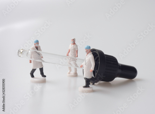 The miniatures of doctors and nurses are placed around the glass dropper stop with the white background. The concept is for the medical research, experiment, and treatment.