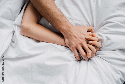 Top view of woman holding hand of boyfriend on bed photo