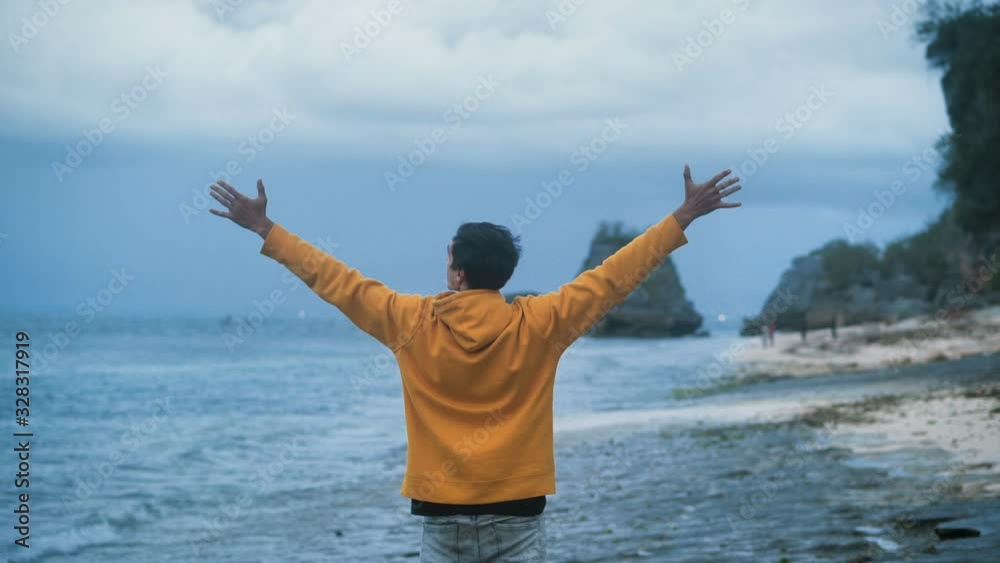 Man traveler raises hands up standing on beautiful tropical beach on the evening. Freedom concept Man traveler raises hands up standing on beautiful tropical beach on the evening. Freedom concept