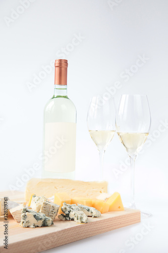 Bottle of white wine two glasses and cheese on a wooden board