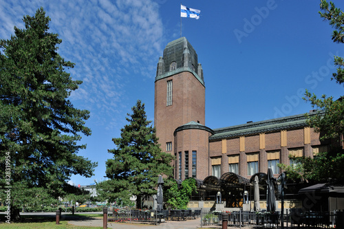 Joensuu City Hall, the Finnish National Flag Flying High in Sky with Pine Trees nearby and Outdoor Cafeteria in Joensuu, North Karelia, Finland in the Morning of June 6,2019 photo