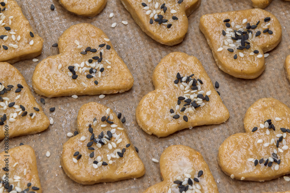 Gingerbread cookie hearts with black and white sesame and sugar on baking paper. The scene of making sweet homemade pastries. Rustic style recipe