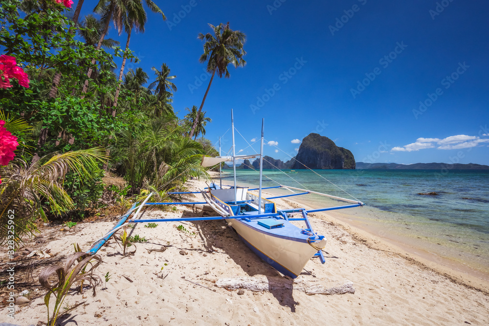 Obraz premium Colored banca boat and vibrant flowers at Las cabanas beach. Surreal landscape in background. Exotic nature scenery in El Nido, Palawan, Philippines