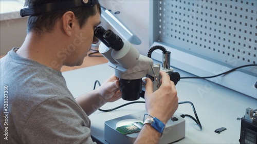 The inventor is testing a prototype that has just been manufactured, he uses a microscope to reveal flaws in the microchip. 