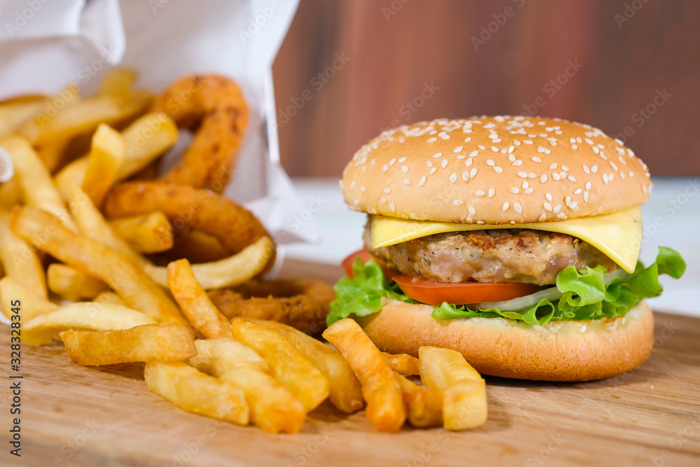Close-up macro of delicious fresh homemade hamburger with cheese, pork, tomato, onion and vegetable on a wooden plate with french fries basket and onion ring. Close-up macro of delicious fresh homemade hamburger with cheese, pork, tomato, onion and vegetable on a wooden plate with french fries basket and onion ring.