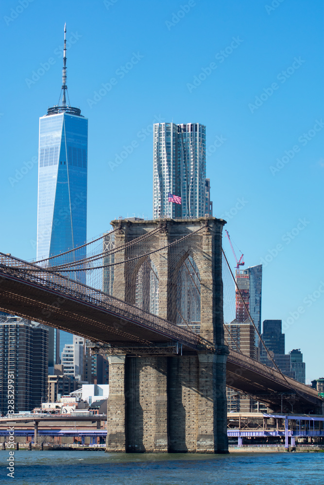 The Brooklyn Bridge with an American Flag over the East River with the Lower Manhattan New York City Skyline
