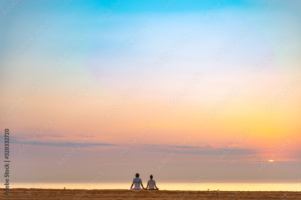 couple doing a relaxing yoga and meditation session on the beach at sunrise with birds and the sun rising