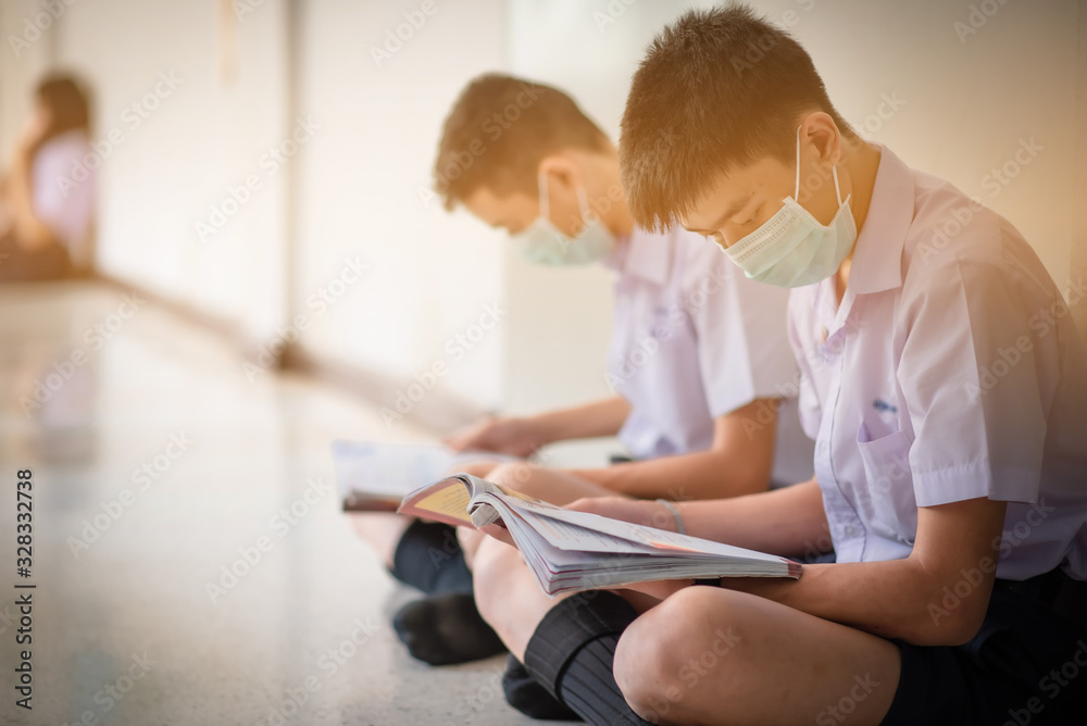 The Asian high school students in the white school uniforms wearing the mask to reading the books to prepare final exams in the midst of Coronavirus disease 2019 (COVID-19) epidemic.