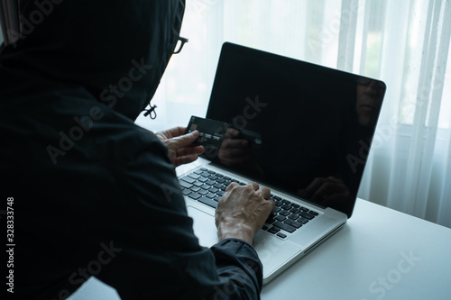Konstfotografi Rearside of man dressing black hood jacket holding credit card and checking password on labtop computer