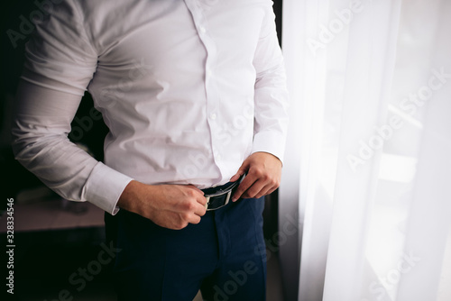 Man tightens the black leather belt on the black pants
