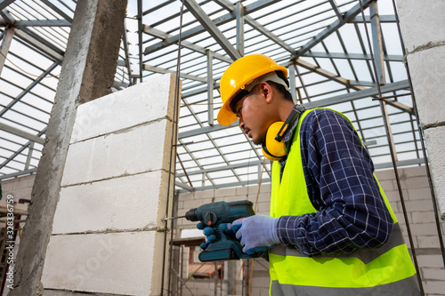 Construction worker use a drill bit,Engineer wearing safety equipment (helmet and jacket) uses a power drill to mount a aerated brick wall.