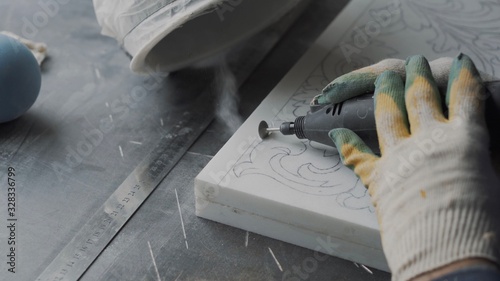 Worker hands with engraving machine do ornament on marble plate