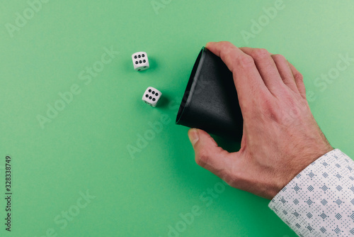 hand of a man using shaker to roll dices against green table background photo