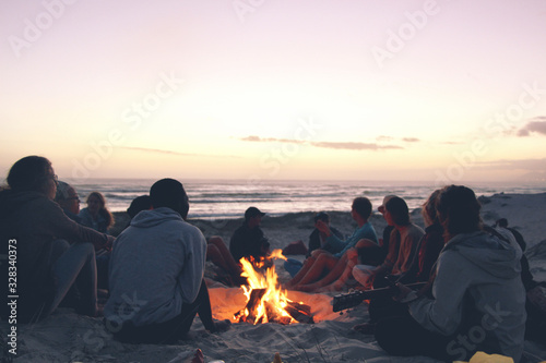 Friends sitting on the beach around a fire during sunset