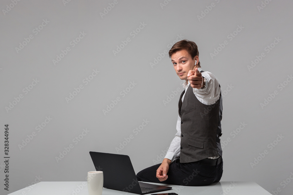 Businessman in a white t-shirt and grey vest sitting pointing at camera with finger Businessman in a white t-shirt and grey vest sitting pointing at camera with finger
